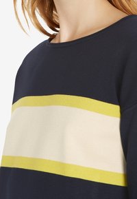 Maglione blu scuro con strisce orizzontali gialle e crema. Realizzato in tessuto morbido con scollatura rotonda e vestibilità morbida.