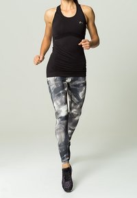 Top deportivo negro sin mangas con un panel texturizado, combinado con leggings grises con un diseño que presenta pinceladas abstractas, y zapatillas negras.