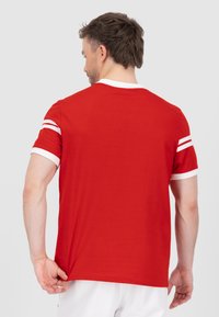 Rode T-shirt met korte mouwen van katoen, met witte strepen op de mouwen en een geribbelde kraag. Het shirt heeft een losse pasvorm en een zachte textuur.