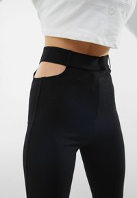 Svarta högmidjade byxor med utskurna sidodetaljer, tillverkade av ett mjukt och stretchigt material. Figursydd design med strömlinjeformad silhuett.