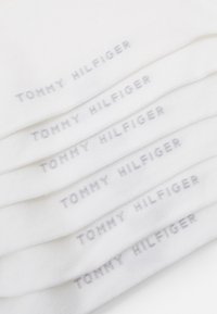 Chaussettes en coton blanc avec un logo gris "TOMMY HILFIGER". Elles présentent une texture lisse et une forme classique de chaussettes montantes, empilées soigneusement.