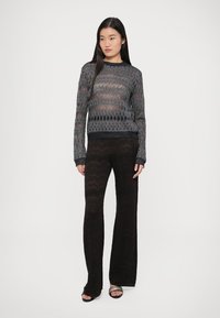 Juodas ir pilkas megztinis su zigzago raštu, derinamas su juodomis plačiomis kelnėmis, demonstruojantis permatomą tekstūrą.