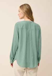 Maglietta verde menta a maniche lunghe realizzata in tessuto leggero, con scollatura rotonda, dettaglio con piega sul retro e polsini con bottoni.
