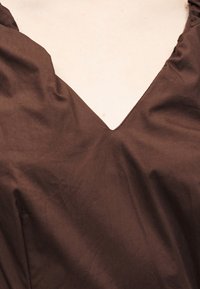 Καφέ ύφασμα με έντονο V-σχήματος ντεκολτέ και ελαφριές ρυτίδες σε λείο υλικό.