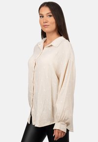 Camicia beige a maniche lunghe con bottoni, colletto, tessuto texturizzato e motivo a pois bianchi. Fit comodo con maniche oversize.