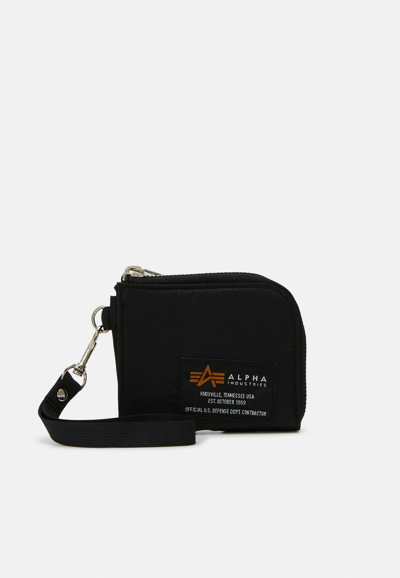 Portefeuille en tissu noir avec une fermeture zippée, doté d'une poignée de poignet et d'un patch logo orange avec du texte sur le devant. Forme rectangulaire compacte.