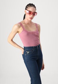 Pink ribbed tank top with lace trim, paired with dark blue high-waisted jeans featuring a patch pocket. Accessories include translucent pink sunglasses.