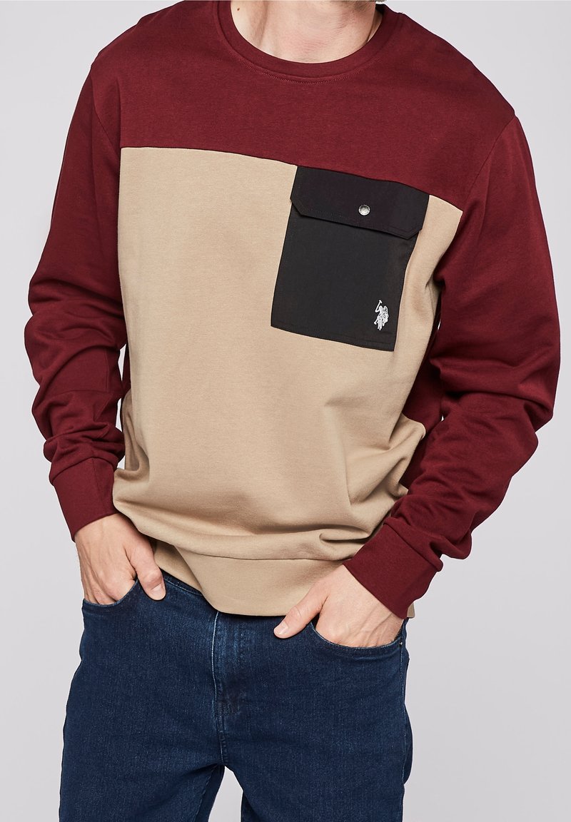 Langärmliges Sweatshirt mit einem dunkelroten oberen Teil, einem beigefarbenen Körper und einer schwarzen Tasche mit Druckverschluss. Weicher Stoff mit legerer Passform.