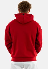 Felpa rossa con cappuccio, maniche lunghe, orlo a costine e dettagli testurizzati sottili. La vista posteriore mostra un colore uniforme e un branding minimale.