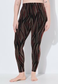 Leggings a motivi neri e rossi con una texture lucida, caratterizzati da una vita alta e un design a zigzag. La composizione del tessuto include una finitura metallica.