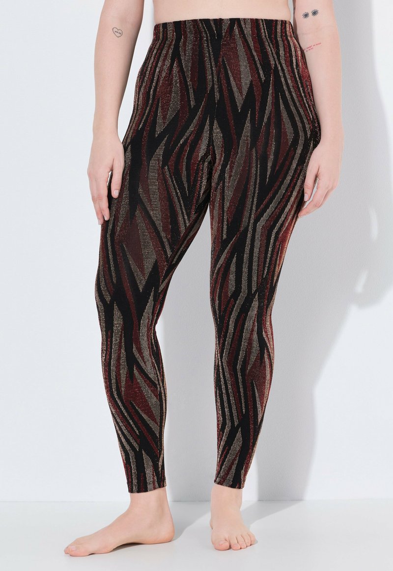Leggings a motivi neri e rossi con una texture lucida, caratterizzati da una vita alta e un design a zigzag. La composizione del tessuto include una finitura metallica.