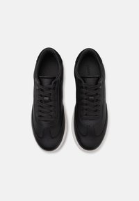 Zwarte leren sneakers met een gestructureerde afwerking, hebben een ronde neus, vetersluiting en een witte rubberen zool.