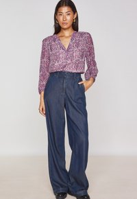 Floral-print blouse in shades of pink with a V-neck and long sleeves, paired with dark blue wide-leg denim trousers and black footwear.