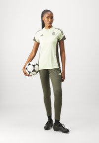 Ljusgrön träningsskjorta med mörkgröna detaljer, parat med matchande åtsittande byxor. Svarta fotbollsskor och en svart-vit fotboll.