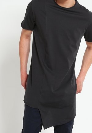 Musta lyhythihainen t-paita, jossa on kaareva helma ja epäsymmetrinen sivusauma. Pehmeää, joustavaa kangasta, rento istuvuus, minimalistinen muotoilu.