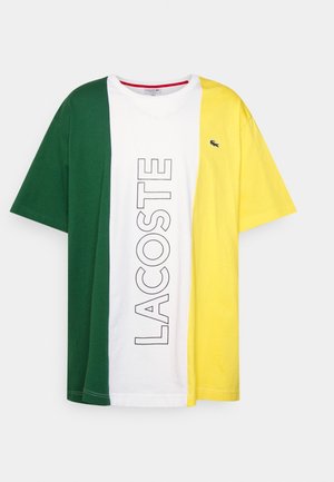Kurzärmeliges T-Shirt mit vertikalen grünen, weißen und gelben Paneelen, "LACOSTE" Schriftzug in der Mitte und kleinem Krokodil-Logo auf dem gelben Paneel.