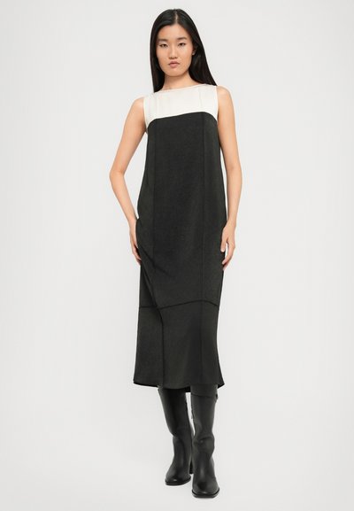 Sleeveless mustas kleit, mille ülemine osa on heledat värvi, tekstuuriga kangast ja põlvekõrgune hem, koos põlvekõrgete mustade saapatega.