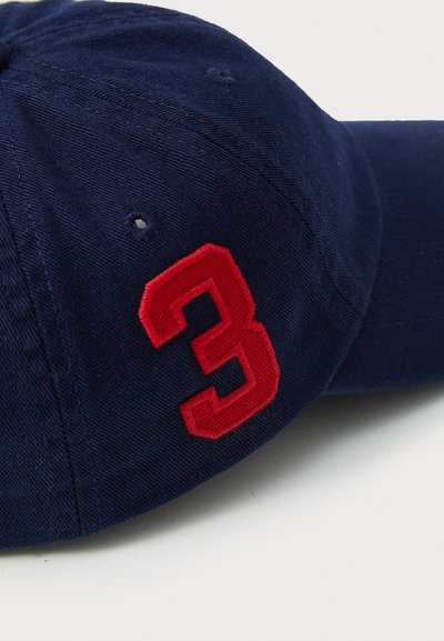 Cappellino blu navy realizzato in cotone con un numero "3" rosso ricamato di lato. Presenta occhielli cuciti per la ventilazione e una visiera curvata.