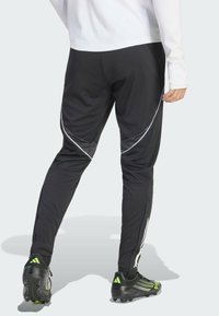 Svarta träningsbyxor med reflexvita detaljer, avsmalnande passform och dragkedjor vid anklarna. Bärs med svarta fotbollsskor med gröna detaljer.