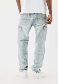 Jeans cargo de color azul claro con un corte holgado, que cuentan con bolsillos laterales y una textura desgastada. Combinados con zapatillas blancas. Se muestra la vista trasera.