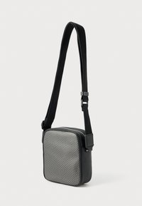 Kwadratowa torebka na pasku z szarym frontem w geometryczny wzór z tkaniny oraz czarnymi bokami z syntetycznej skóry; regulowany pasek i zamek błyskawiczny.