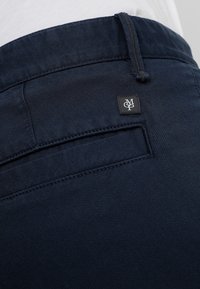 Pantalones azul marino con un tejido texturizado, un bolsillo trasero y una pequeña etiqueta de logo negra cerca de la cintura. Diseño liso y ajustado.