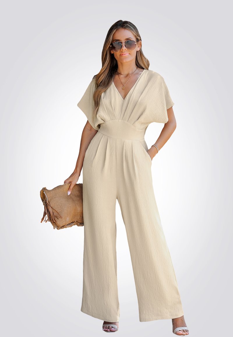 Beige jumpsuit met een gestructureerde afwerking, v-hals en wijde benen; gecombineerd met een bruine clutch met franjeranden.