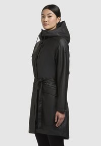 Zwarte regenjas met capuchon, aangesloten taille en knopen. Beschikt over een gladde textuur en zijzakken, ontworpen voor bescherming tegen het weer.