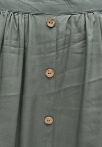 Γκρι ύφασμα μαζεμένο στο πάνω μέρος με τρία κάθετα ευθυγραμμισμένα στρογγυλά καφέ κουμπιά, ραμμένα με δύο τρύπες το καθένα.