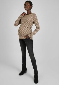 Gestreiftes Langarmoberteil in Braun und Beige, kombiniert mit schwarzen Skinny Jeans und schwarzen Stiefeletten. Glatte Textur, taillierte Passform und abgerundeter Saum.