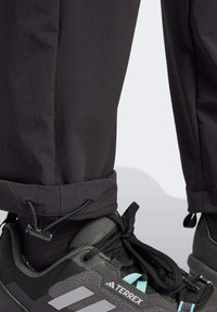 Mustat housut, joissa on joustavat resorit, yhdistettyinä mustiin ja harmaisiin vaelluskenkiin, joissa on turkoosinsinisiä yksityiskohtia ja teksturoitu päällinen.