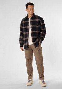 Camisa de flanela xadrez azul-marinho com detalhes em castanho e laranja, combinada com calças cargo bege com bolsos e costuras resistentes. Tênis incluídos.