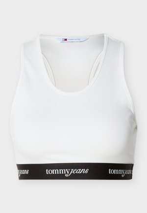 Balts sporta krūšturis ar melnu elastīgu joslu apakšā, uz kuras ir atkārtots baltu burtiem "tommy jeans" zīmola nosaukums.