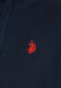 Navy blue knit fabric with a small embroidered red logo of a polo player on horseback in the center.