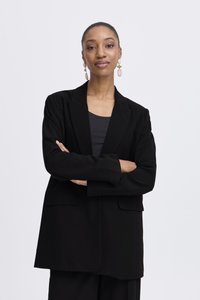 Črni blazer ohlapnega kroja z dvema prednjima žepoma in zarezanimi ovratniki, v kombinaciji s sivim topom in širokimi črnimi hlačami. Gladek tekstil.