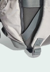 Šedý batoh s hladkým látkovým telom, sieťovanou časťou pre priedušnosť a nastaviteľnými popruhmi so zapínaním na sponu.