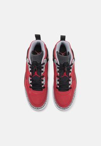 Paire de baskets Air Jordan rouges, noires et grises avec des lacets noirs et des semelles intermédiaires blanches à motifs, vues de dessus sur un fond blanc.