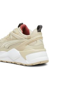 Beżowe sneakersy z teksturowaną siateczką i syntetycznymi akcentami. Posiadają białą podeszwę pośrodkową, czerwoną wyściółkę i szary uchwyt na pięcie. Zauważalny detal z logo.