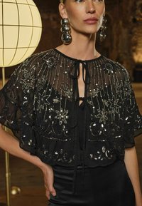 Must mustri kapuuts, millel on detailne hõbedane kaunistus, kaeluses sidumine, kellukesed varrukad ja keerukad tähtede mustrid.