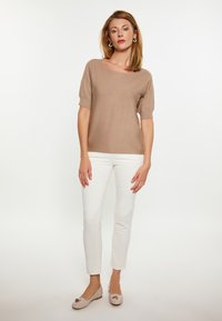 Vaahto beige'n neulottu lyhythihainen toppi, joka on yhdistetty valkoisiin slim-fit-housuihin ja vaaleisiin tasapohjaisiin kenkiin, joissa on koristeellinen yksityiskohta.