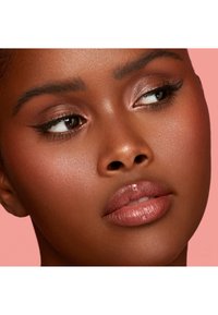 Nærbilde av et ansikt med glatt, dyp brun hud. Kjennetegn inkluderer fremhevede kinnben, glansfulle nude lepper og definert eyeliner mot en rosa bakgrunn.