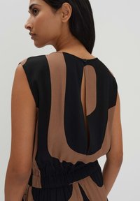 Mouwloze kleding met een kleurblokontwerp in bruin en zwart. Heeft een achterste sleutelgatopening die wordt vastgezet met een knop en een elastische tailleband.