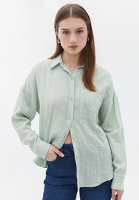 Lichtgroen overhemd met knopen, gemaakt van een textuurstof, met lange mouwen, een enkele borstzak en een ontspannen pasvorm, gecombineerd met donkere jeans.