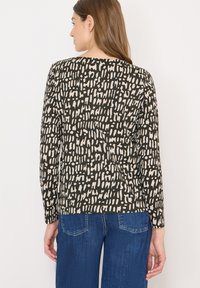 Czarna bluzka z długim rękawem z białym abstrakcyjnym wzorem. Wykonana z miękkiego materiału, posiada okrągły dekolt i luźny krój.