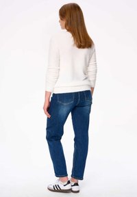 Witte fluffy trui, blauwe jeans en witte sneakers met zwarte accenten. Achteraanzicht toont ribbelmanchetten en de losse pasvorm van de jeans.