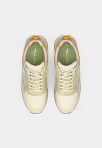 Une paire de baskets beige, vert clair et orange à lacets avec des semelles intérieures vertes étiquetées "Tamaris", présentée en vue de dessus sur fond blanc.