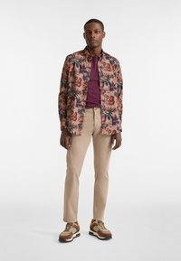 Floral-patterned long-sleeve shirt in muted pink, paired with a maroon t-shirt, beige pants, and multicolor sneakers.