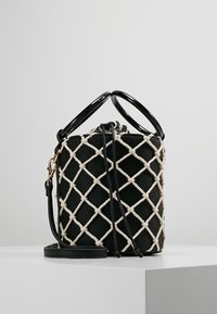 Czarna torebka na ramię z pikowanym wzorem, podkreślającym krzyżujące się paski w kolorze kremowym. Posiada dwa okrągłe czarne uchwyty oraz odpinany pasek.