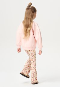 Różowy oversize'owy sweter z prążkowanymi mankietami i dołem;spodnie w kwiaty w rozkloszowanym kroju w delikatnych pastelowych kolorach. Brązowe buty wsuwane.