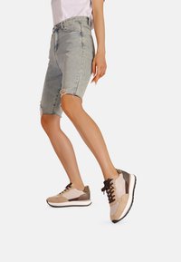 Sneaker beige e marroni realizzati in materiali scamosciati e in rete, con un accento a stampa leopardata e lacci tradizionali. Design atletico casual.